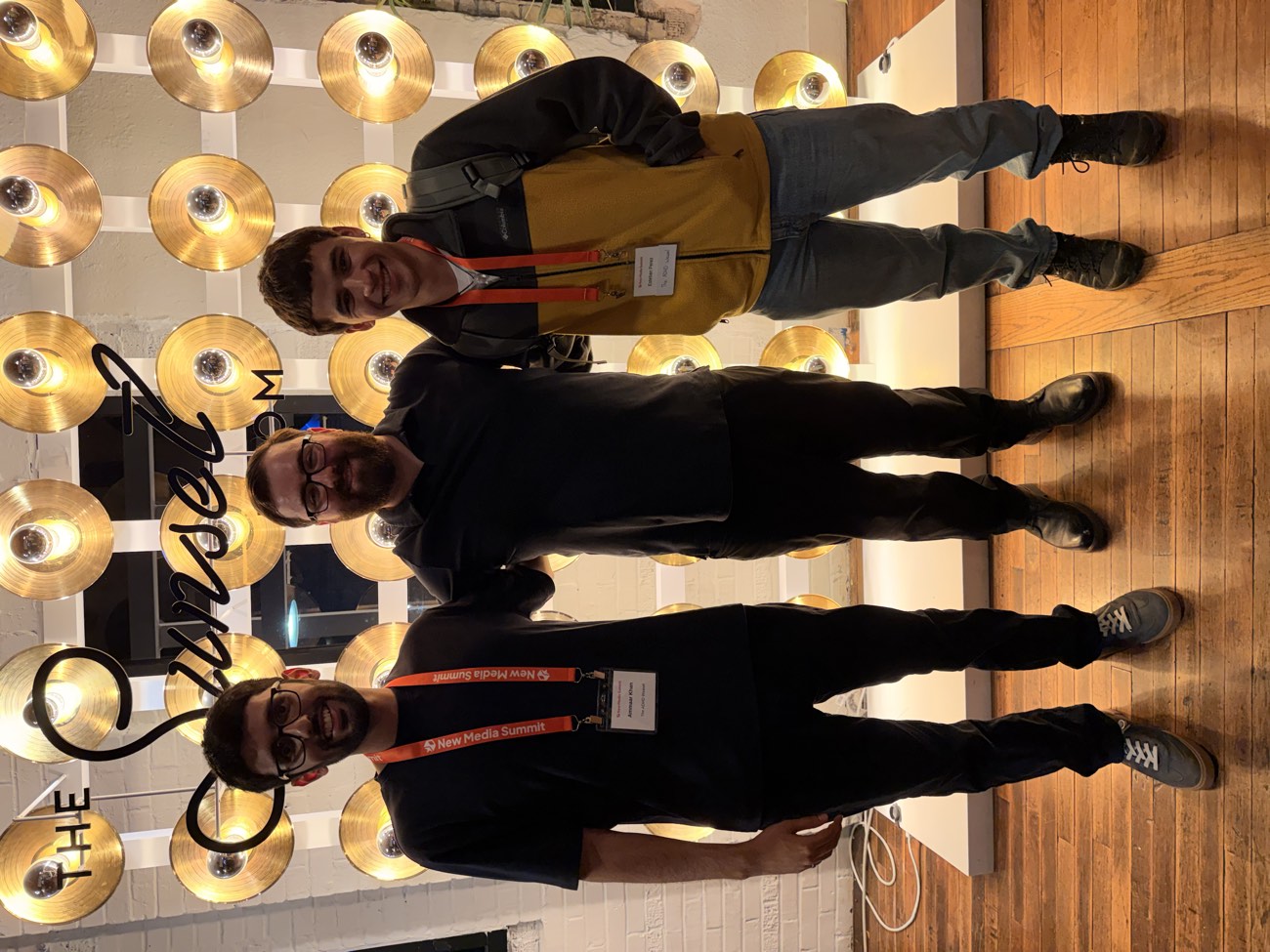 Ammaar Khan, Matt McGarry, and Esteban Perez standing together in front of a wall of gold records at the New Media Summit
